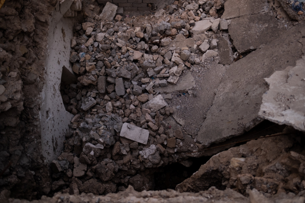 Zusammengebrochenes Gebäude mit einem großen Loch im Boden, umgeben von Schutt und einem sichtbaren Rohr auf der linken Seite, das Erdbebenschäden anzeigt.